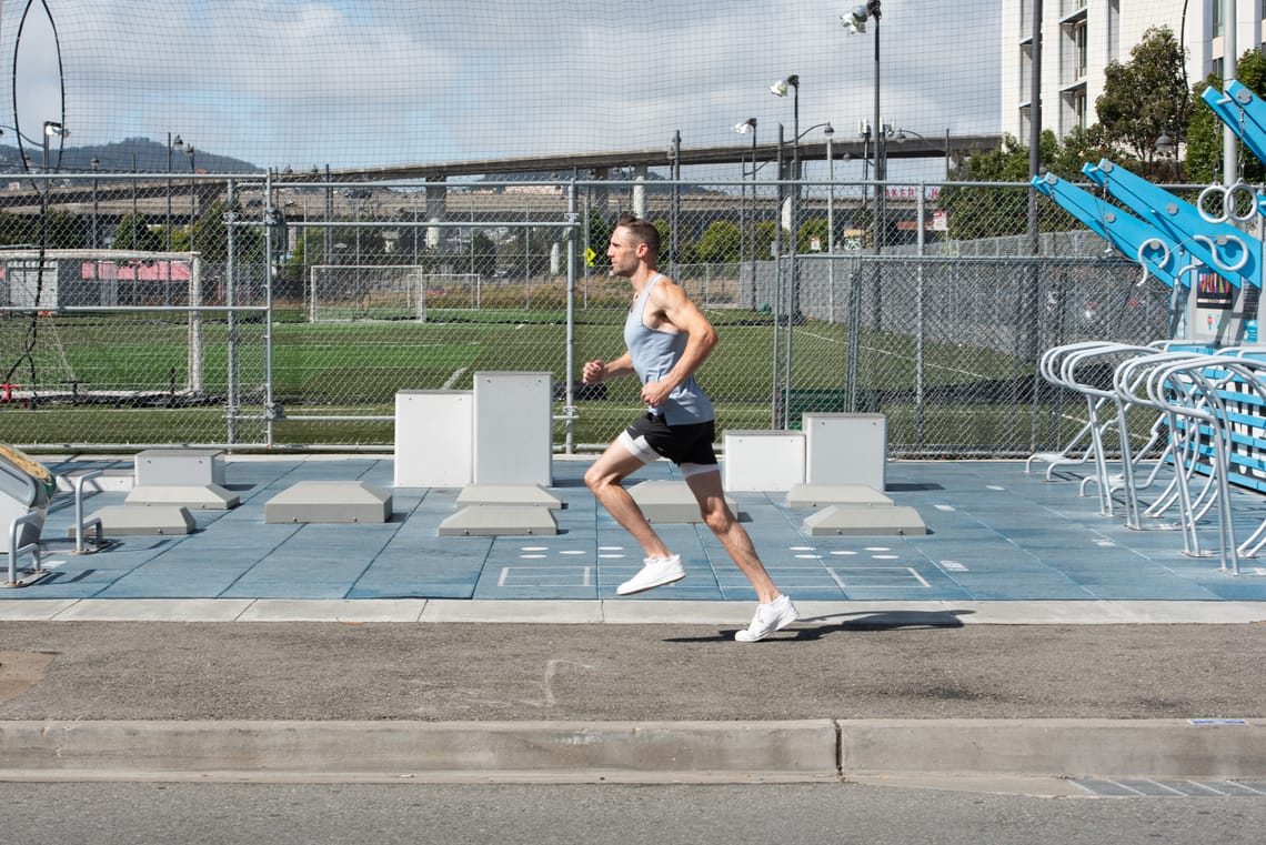 Model running along the sidewalk in front of an outdoor fitness park